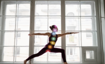 Woman practicing yoga in warrior pose with glowing chakra points aligned along her body, symbolizing mind-body healing and inner growth.