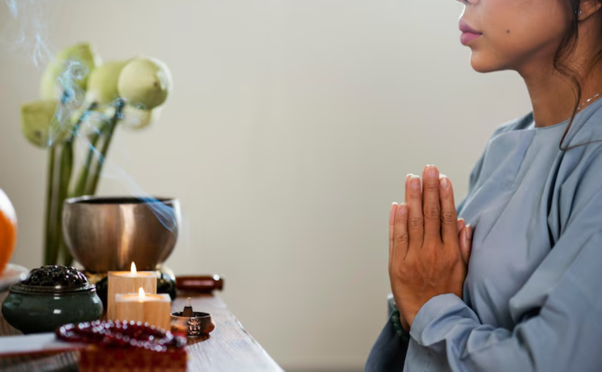 A woman in a peaceful posture with folded hands, seated beside candles and incense visually representing the healing journey through Ho’oponopono practice.